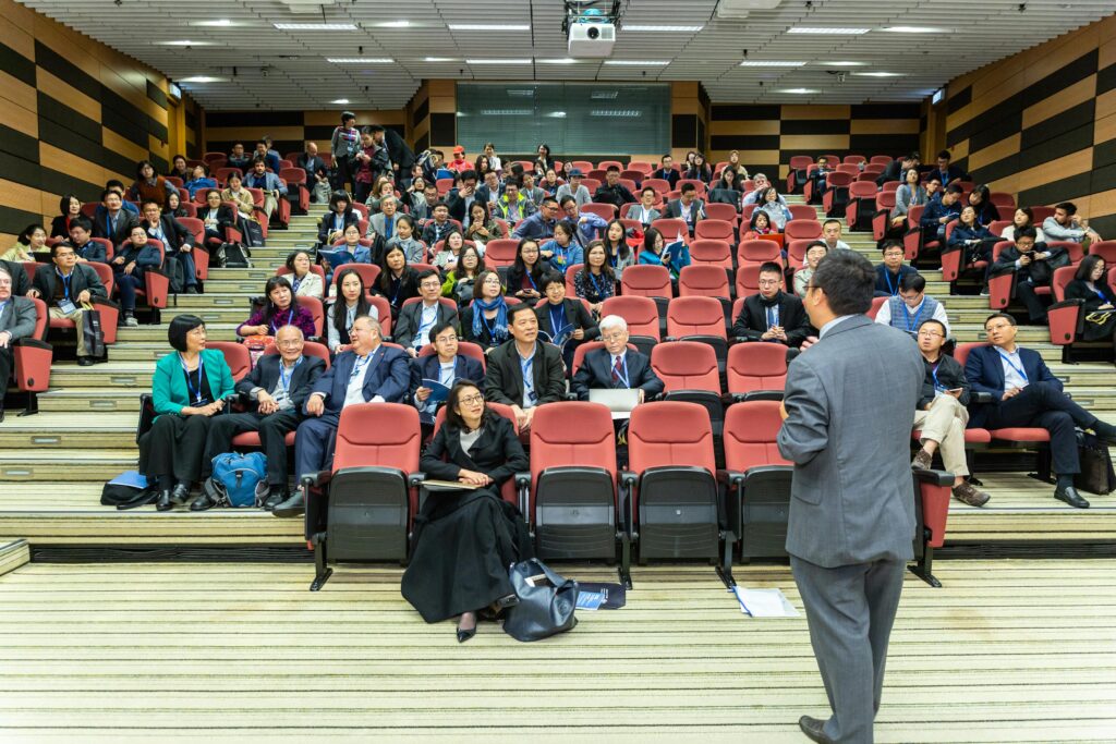 Professional setting of a business conference with attendees and a presenter in an auditorium.