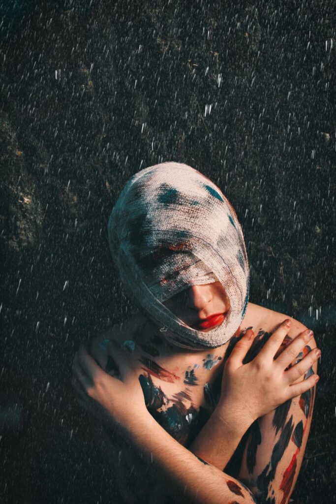 From above of melancholic injured anonymous female with head and face covered with bandage and paints on body