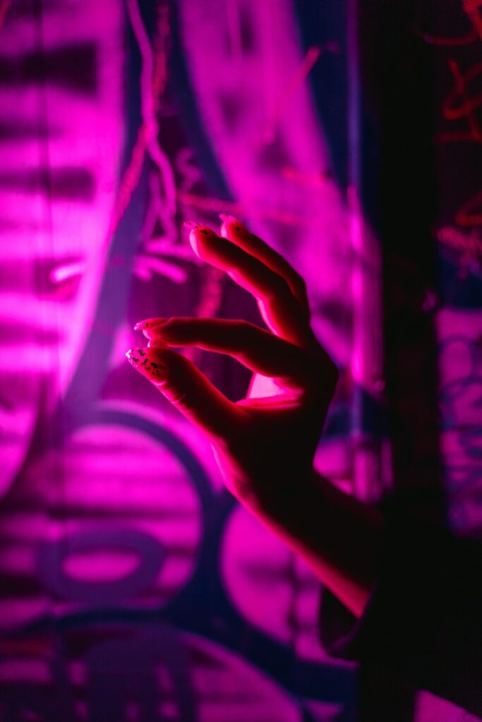 A silhouette of a hand gesturing against vibrant neon pink graffiti background.